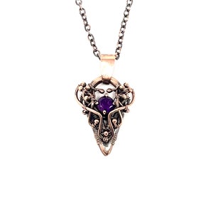 May include: A silver and copper wire wrapped pendant with a purple amethyst gemstone in the center. The pendant is shaped like a teardrop and hangs from a silver chain.