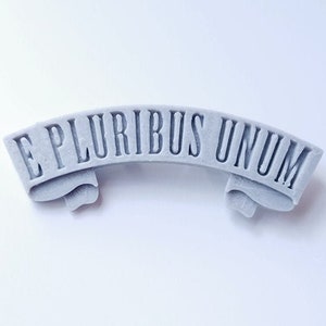 May include: A gray, 3D printed banner with the text "E PLURIBUS UNUM" in a classic serif font.