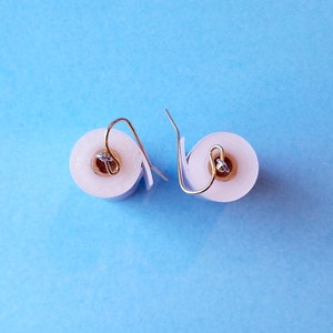 May include: A pair of white toilet paper roll earrings with silver hooks. The earrings are on a blue background.