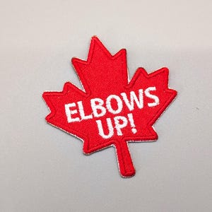 May include: Red felt Canadian maple leaf patch with white embroidered text that reads "ELBOWS UP!"