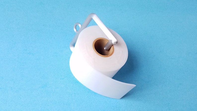 May include: A white toilet paper roll on a silver metal holder against a light blue background.