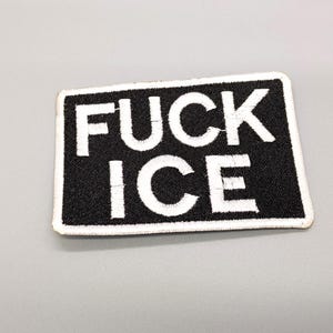 May include: A rectangular black and white embroidered patch. The patch features the words "FUCK ICE" in bold white capital letters. The patch has a white border and is set against a gray background.