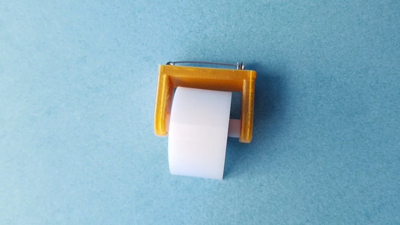 May include: A small, yellow plastic dispenser with a white tape roll. The dispenser has a metal pin on top.