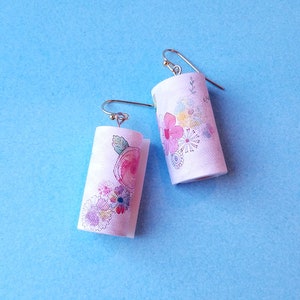 May include: A pair of white cylinder earrings with a floral design. The earrings have silver hooks.