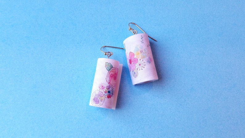 May include: A pair of white cylinder earrings with a floral design. The earrings have silver hooks.