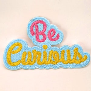 May include: A blue fabric patch with the words "Be Curious" embroidered in yellow and pink thread.