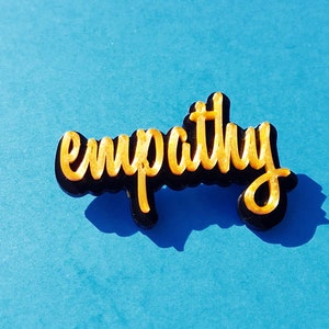May include: A gold-colored word "empathy" is written in a stylized font on a black background. The word is on a blue surface.
