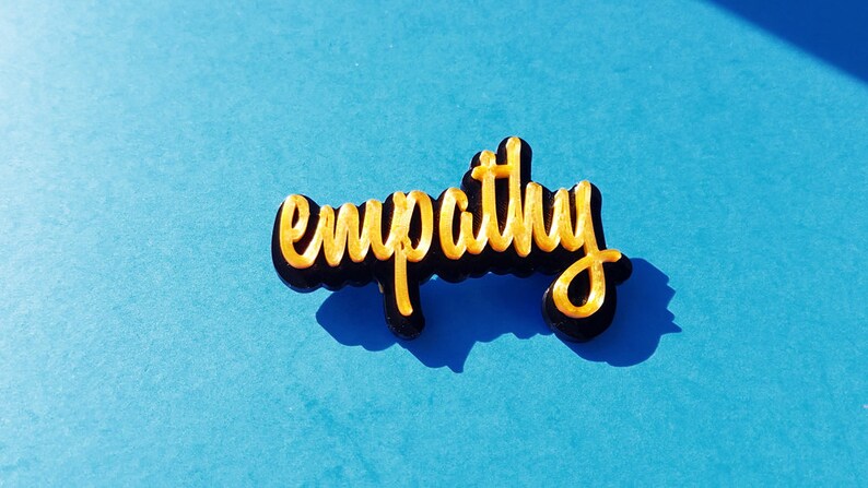 May include: A gold-colored word "empathy" is written in a stylized font on a black background. The word is on a blue surface.