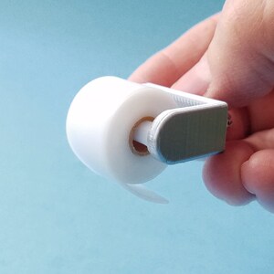 May include: A white plastic toilet paper holder with a roll of white toilet paper. The holder is designed to be mounted on a wall.
