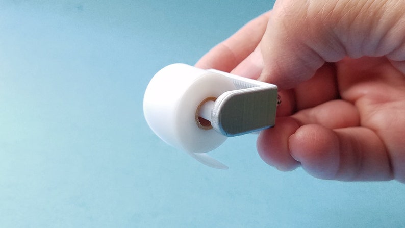 May include: A white plastic toilet paper holder with a roll of white toilet paper. The holder is designed to be mounted on a wall.