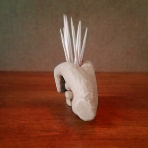Pu&ograve; includere: Una scultura di mano in ceramica con una superficie testurizzata, che tiene un mazzo di stuzzicadenti.