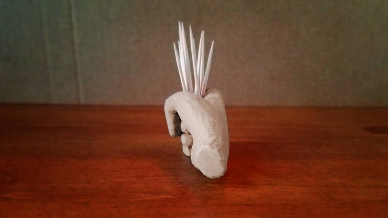 Pu&ograve; includere: Una scultura di mano in ceramica con una superficie testurizzata, che tiene un mazzo di stuzzicadenti.