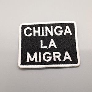 May include: Black rectangular patch with white embroidered text that reads "CHINGA LA MIGRA". The patch has a white border and is set against a gray background. The text is in a bold, sans-serif font.