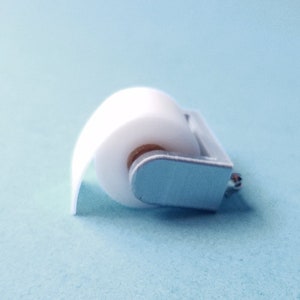May include: A white paper roll on a silver metal holder. The holder has a small silver knob on the side.