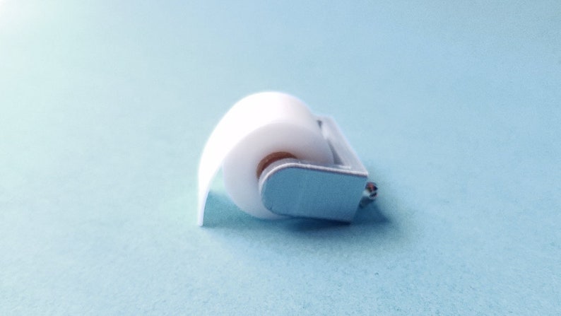 May include: A white paper roll on a silver metal holder. The holder has a small silver knob on the side.