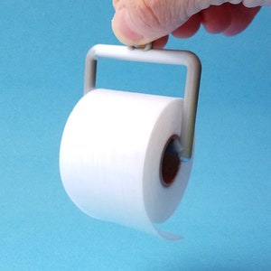 May include: A white toilet paper roll on a gray plastic holder with a handle. The holder is being held by a hand.