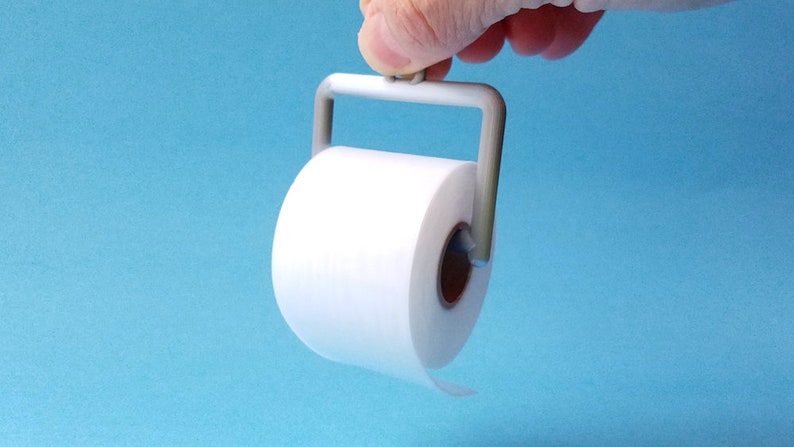 May include: A white toilet paper roll on a gray plastic holder with a handle. The holder is being held by a hand.