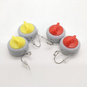 May include: A pair of earrings featuring miniature curling stones. The stones are gray with yellow and red handles.