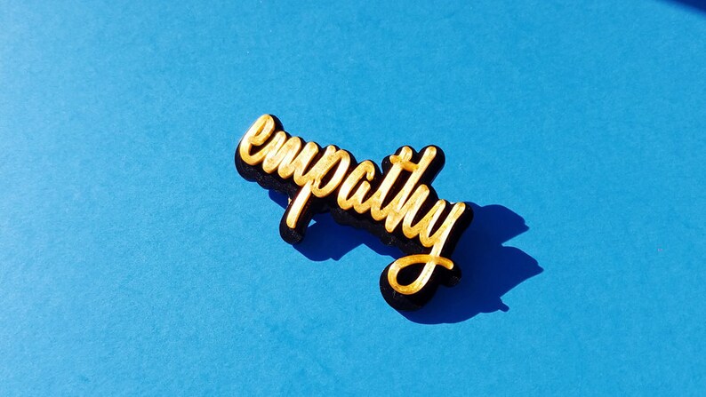 May include: A gold-colored word "empathy" is written in a cursive font on a black background. The word is on a blue surface.