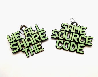 May include: A pair of green and black earrings with a pixelated design. The left earring says "WE ALL SHARE THE" and the right earring says "SAME SOURCE CODE".