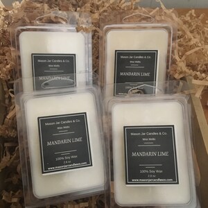 May include: Four clear plastic packages of Mandarin Lime wax melts. Each package has a black and white label with the text "Mason Jar Candles & Co." and "MANDARIN LIME". The wax melts are white and sit in a bed of brown packing material.