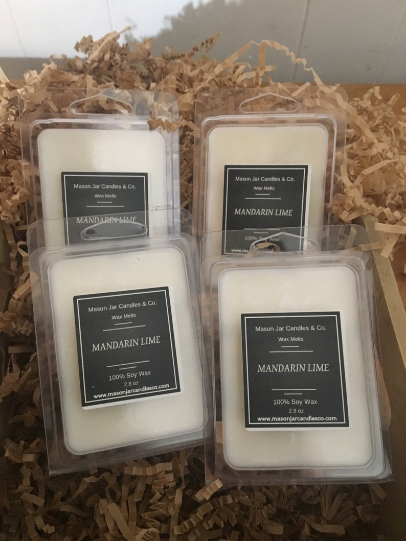 May include: Four clear plastic packages of Mandarin Lime wax melts. Each package has a black and white label with the text "Mason Jar Candles & Co." and "MANDARIN LIME". The wax melts are white and sit in a bed of brown packing material.
