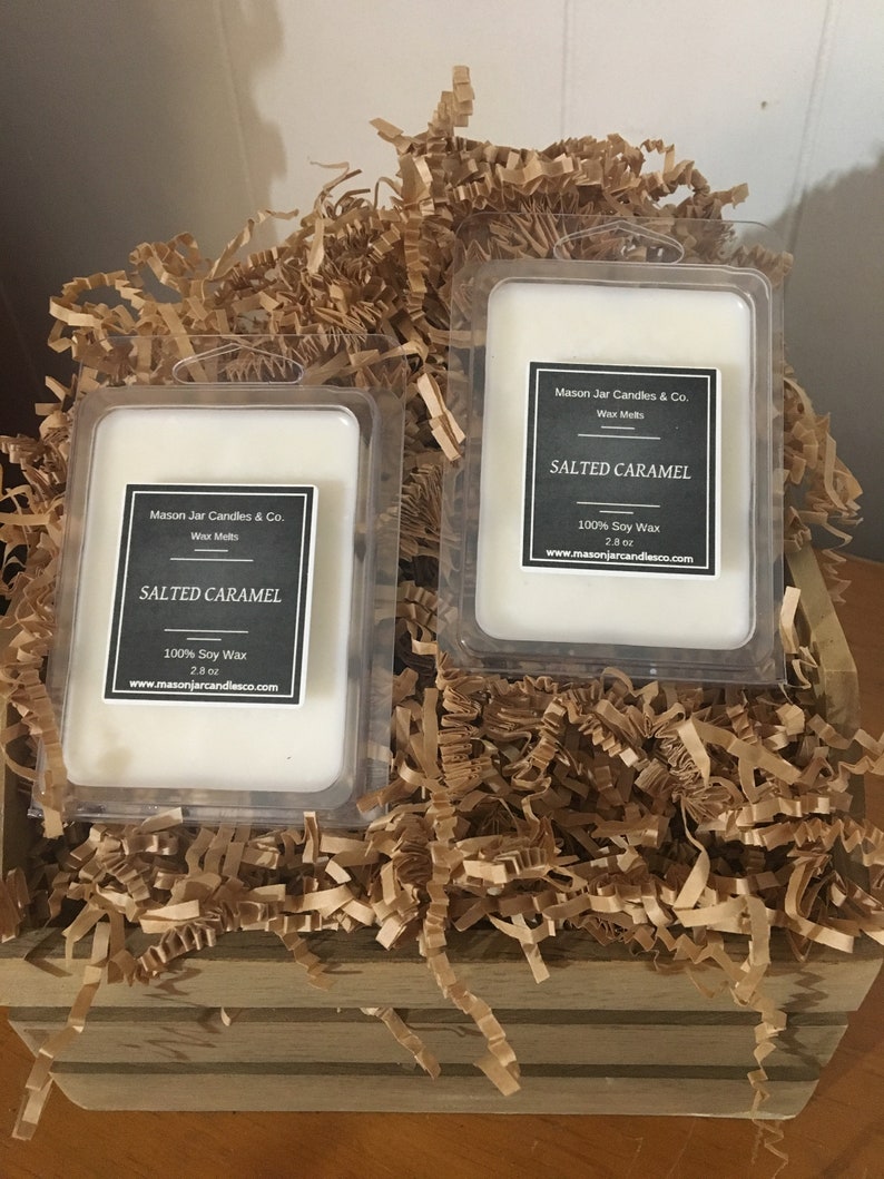 May include: Two rectangular wax melt containers labeled "Salted Caramel" from Mason Jar Candles & Co. are nestled in a wooden crate filled with brown paper shreds. Each container holds a white wax melt and includes the text "100% Soy Wax" and "2.8 oz".