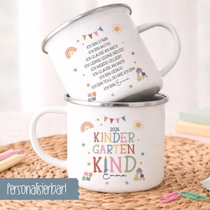 Könnte beinhalten: Zwei weiße Emaille-Tassen, die vertikal gestapelt sind. Die obere Tasse zeigt deutsche Affirmationen und einen Regenbogen. Die untere Tasse zeigt den Text 2026 KINDER GARTEN KIND, einen Regenbogen, eine Sonne und Bauklötze. Beide sind mit Emma personalisiert.