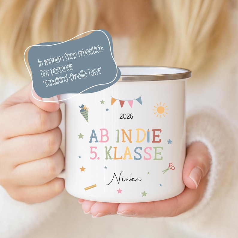 May include: White enamel mug with a silver rim, featuring colourful text and illustrations. The mug has the words "AB IN DIE 5. KLASSE" and the name "Nieke". Includes a banner, sun, stars, and the year 2026.