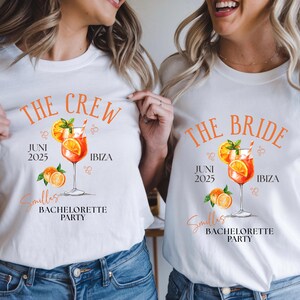 May include: White t-shirts with orange text and a cocktail graphic. One shirt reads "THE CREW" and the other "THE BRIDE". Both shirts include "JUNI 2025", "IBIZA", and "Smillas BACHELORETTE PARTY".