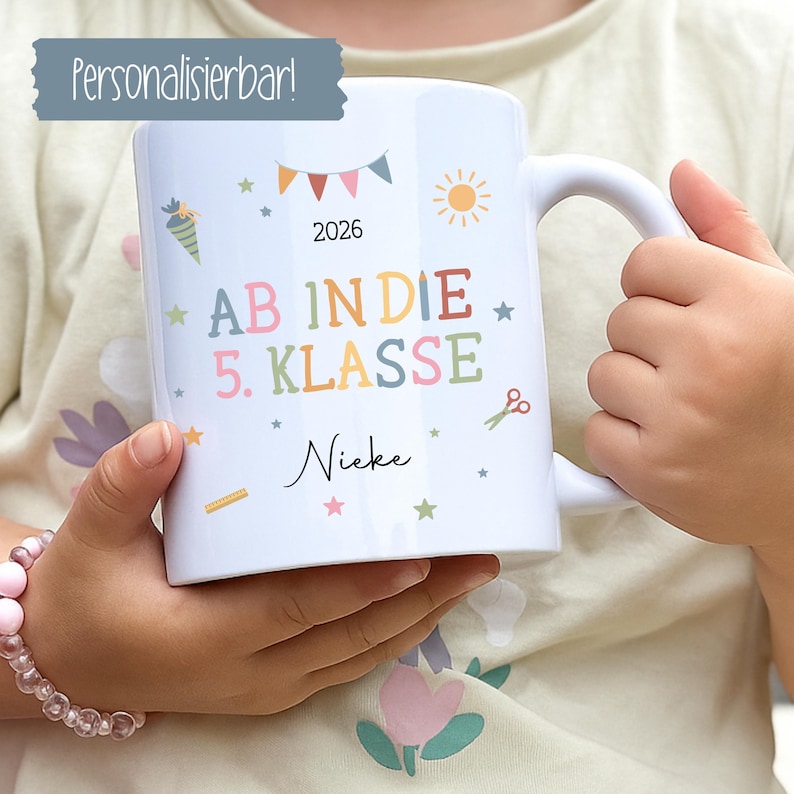 May include: White ceramic mug with colourful text and illustrations. The mug features the text "AB IN DIE 5. KLASSE" and the name "Nieke". Adorned with stars, a sun, scissors, and a banner, it's a personalised gift for a student.