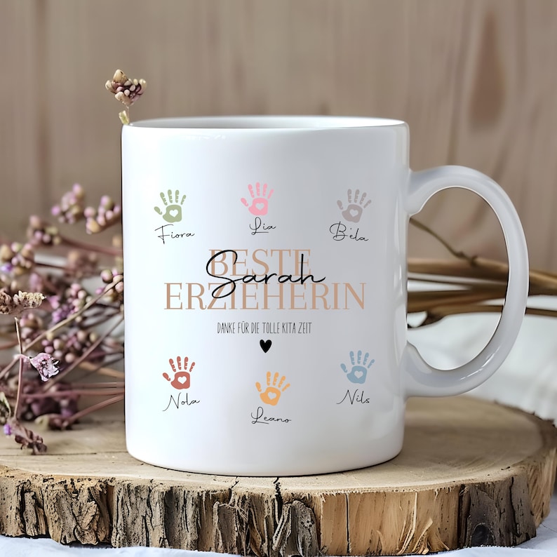 May include: White ceramic mug with a handle, decorated with colourful handprints and the text "Beste Erzieherin Sarah". The mug also includes the names of children. A thoughtful gift for a teacher.