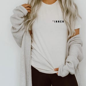 Könnte beinhalten: Ein weißes T-Shirt mit dem Wort "*INNEN" auf der Vorderseite.