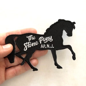 May include: Black embroidered patch in the shape of a horse with the text "The Stone Pony AP, N.J." in white script. The horse is rearing up on its hind legs, with a detailed outline.