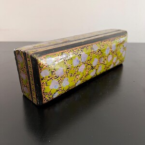 May include: A small, rectangular box with a black base and a green and purple floral design. The box has a glossy finish and gold accents.