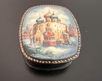 May include: A small, black wooden box with a painted scene of a church in a snowy landscape. The lid is decorated with a gold trim and the words "Палац-Софиевка 1800" are written on the bottom.
