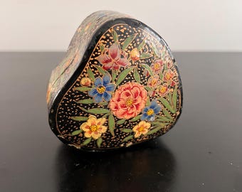 May include: A black heart-shaped box with a floral design. The box is painted with colorful flowers and leaves on a black background.