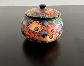 Pode incluir: Uma caixa de madeira preta com um design floral. A caixa é decorada com flores coloridas em tons de rosa, amarelo, azul e verde. A tampa da caixa tem um pequeno botão.