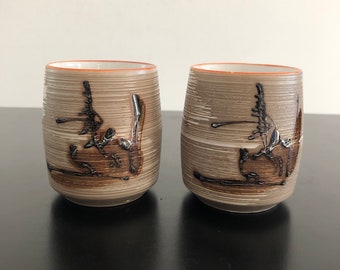 Puede incluir: Dos tazas de té de cerámica con un esmalte marrón claro y diseños abstractos negros. Las tazas tienen una forma ligeramente redondeada y una abertura ancha.