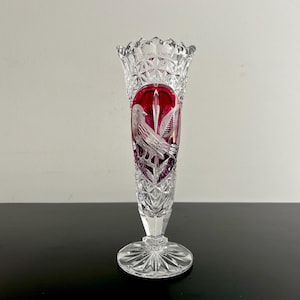 Puede incluir: Un florero de vidrio tallado transparente y rojo rubí con un borde festoneado y un cuerpo con patrón de diamantes. El centro del florero muestra un panel ovalado con un diseño grabado de un pájaro posado en una rama sobre un fondo rojo.