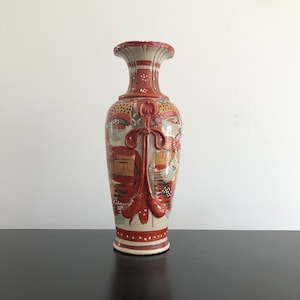 Puede incluir: Un jarrón de cerámica con fondo blanco y diseños pintados en rojo, naranja y negro. El jarrón tiene una boca ancha y un cuello estrecho.