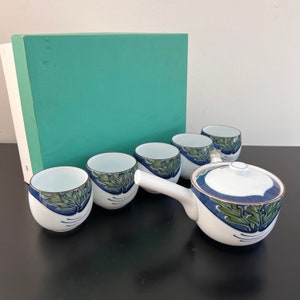 May include: A white tea set with a blue and green floral design. The set includes a teapot and five cups. The teapot has a lid and a handle. The cups are all the same size and have a rounded shape. The set is in a teal box.