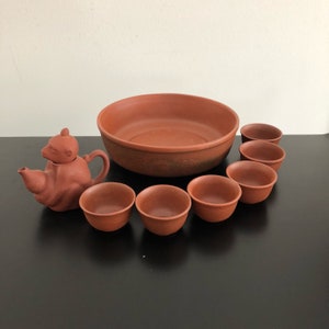 以下が含まれることがあります： テラコッタ製のティーセット。猿の形をした蓋が付いたティーポット、大きなボウル、6つの小さなカップが含まれています。セットは暖かく赤みがかった茶色で、粘土で作られているようです。ティーポットには注ぎ口と取っ手が付いています。