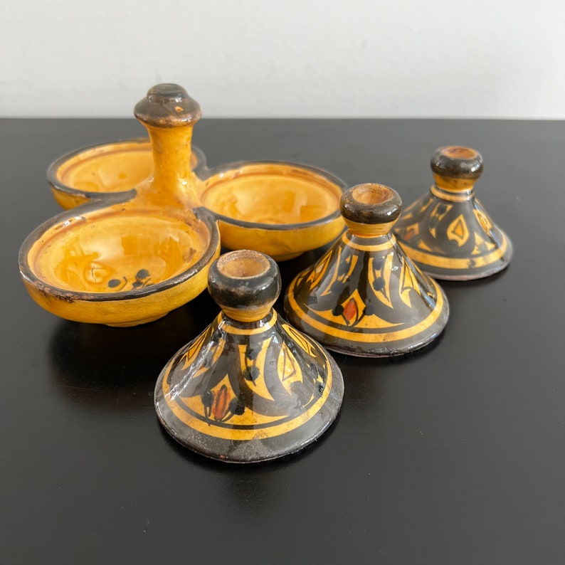 May include: A yellow ceramic condiment set with three individual bowls and lids. The bowls are decorated with black and orange geometric patterns.