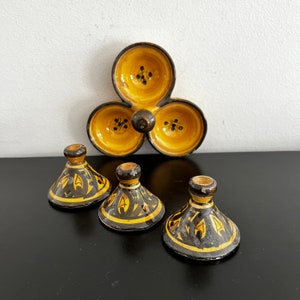 May include: A set of four ceramic condiment dishes. The dishes are yellow with black floral designs. Three of the dishes are small and have lids. The fourth dish is larger and has three sections. The dishes are on a black surface.