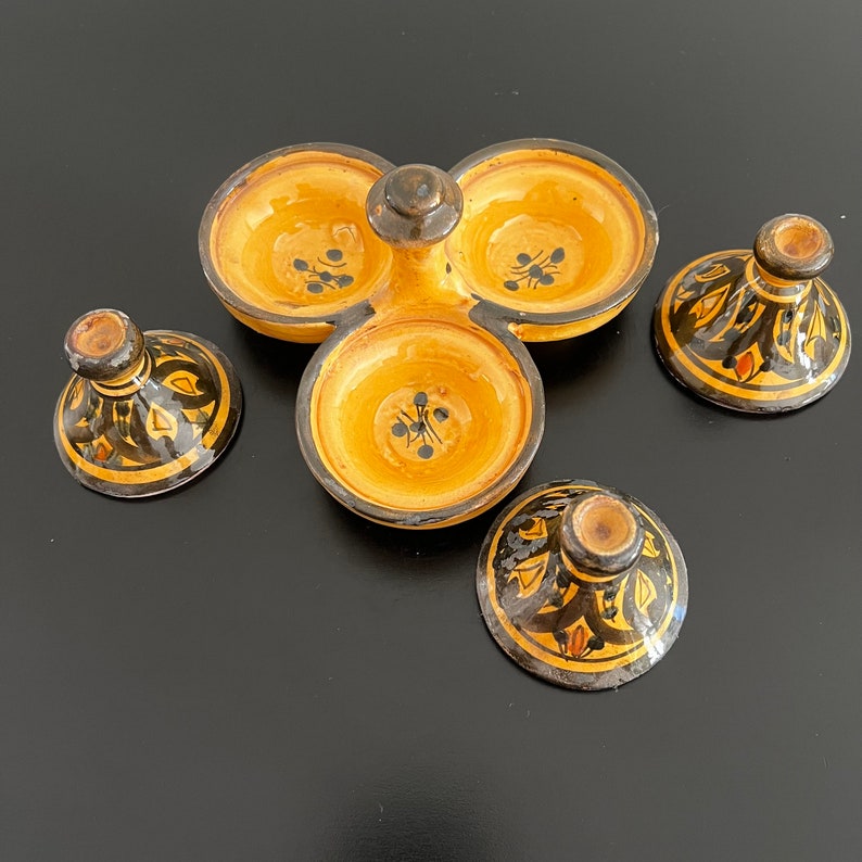 May include: A set of four ceramic bowls with lids. The bowls are yellow with black and orange designs. The lids are also yellow with black and orange designs. The bowls are arranged in a circle with the lids on top.