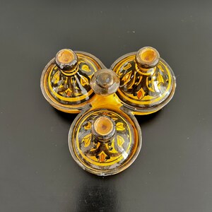 May include: A set of three small ceramic bowls with black and yellow geometric designs. The bowls are arranged in a triangular shape and have a glossy finish.