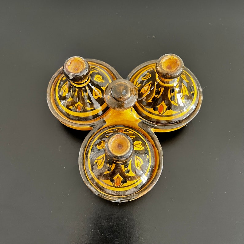 May include: A set of three small ceramic bowls with black and yellow geometric designs. The bowls are arranged in a triangular shape and have a glossy finish.