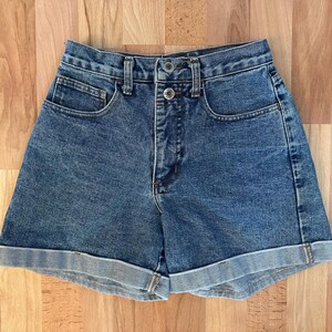 Peut inclure: Shorts en jean bleu taille haute de conception classique. Les shorts ont une fermeture boutonnée et zippée, des poches avant et arrière et des ourlets retroussés. Le vêtement est en tissu denim de délavage moyen.