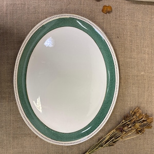 May include: A white oval serving platter with a green and gold border. The border has a delicate floral pattern.